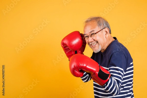 Fototapeta Portrait Asian old man wearing glasses wear two red boxing gloves studio shot isolated yellow background, smiling happy elderly man gray haired healthy fighter lifestyle concept