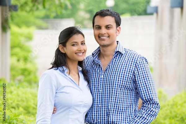 Obraz Closeup portrait, attractive wealthy successful couple in blue shirt and striped outfit holding each other smiling, isolated outside green trees background.