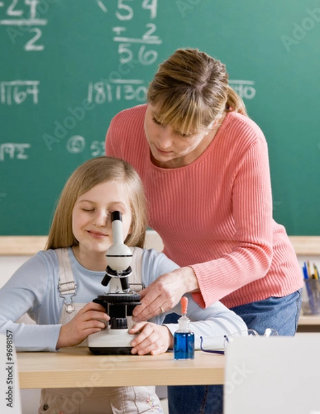 Fototapeta Teacher helping student adjust microscope in classroom