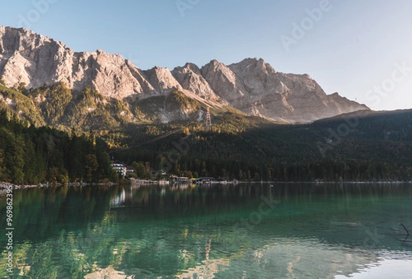 Obraz A landscape of Lake Eibsee in Bavaria, southern Germany. The water reflects the distant shore, green forest and mountains of the Alps that climb in the distance. The sky is blue and clear.