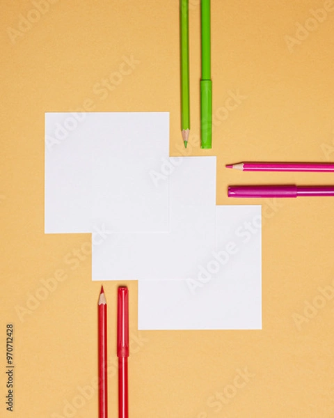 Fototapeta three square sheets of paper with pens and pencils on orange background