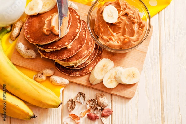 Fototapeta 
hearty and healthy breakfast , American pancakes with bananas , nuts , peanut butter and milk on a wooden background