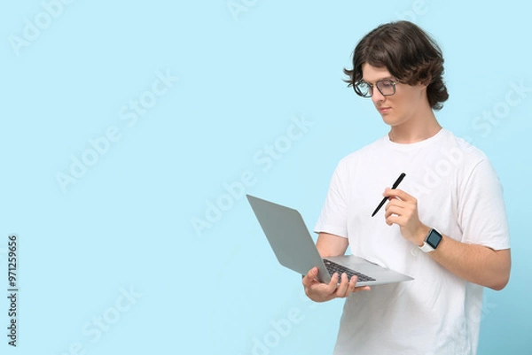 Fototapeta Male programmer in eyeglasses with laptop and pen on blue background