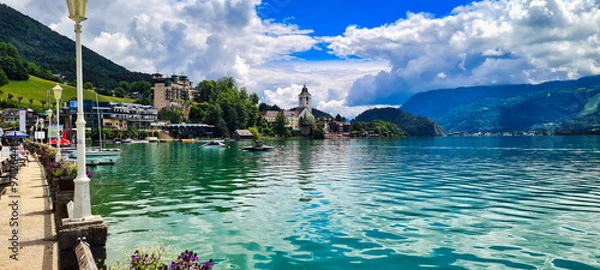 Fototapeta A picturesque view of Wolfgangsee, Austria, with crystal-clear waters, charming lakeside architecture, and the backdrop of lush green mountains. A perfect destination for relaxation, water sports, and