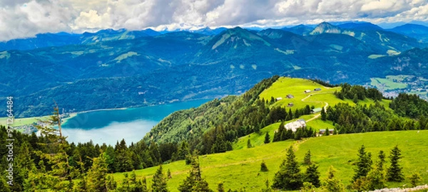Fototapeta A breathtaking view from the Schafberg in Austria, showcasing lush green meadows, mountain ridges, and the stunning Wolfgangsee in the distance. The perfect spot for hiking and soaking in the panorami