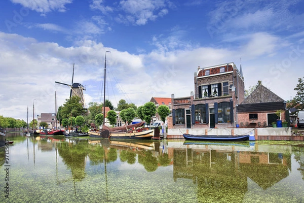 Obraz Smooth green canal with moored boats and monumental houses in the old town of Gouda, The Netherlands.