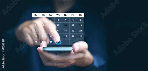 Fototapeta Planning and time management concept. A man manages his time using virtual screen calendar interface on his smartphone to highlight the date to remind him about important work, meeting, or agenda