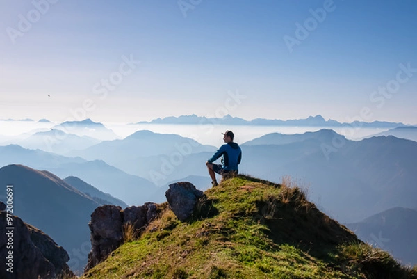 Fototapeta Silhouette of hiker man in alpine landscape of Gailtal Alps, Carinthia, Austria. Panoramic view of majestic hazy mountain ridges of Julian Alps, Karawanks, Carnic Alps. Peaceful tranquil atmosphere