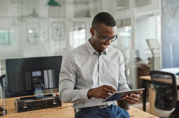 Fototapeta Smiling African businessman leaning on an office desk using a tablet