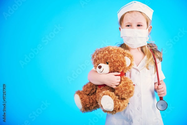 Obraz Beautiful doctor, nurse examines teddy bear on a blue background