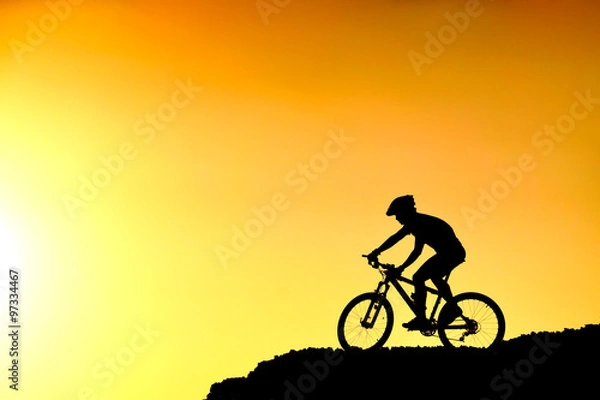 Fototapeta A cyclist riding down the hill with sunset silhouette