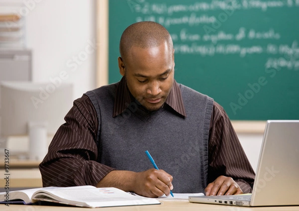 Fototapeta Teacher with laptop grading papers in school classroom