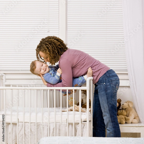 Fototapeta Devoted mother laying son down into crib for nap in bedroom