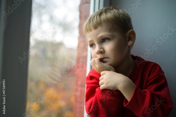 Fototapeta small boy sitting near window and thnking about something