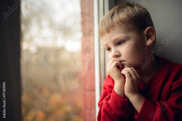 Fototapeta small boy sitting near window and thnking about something