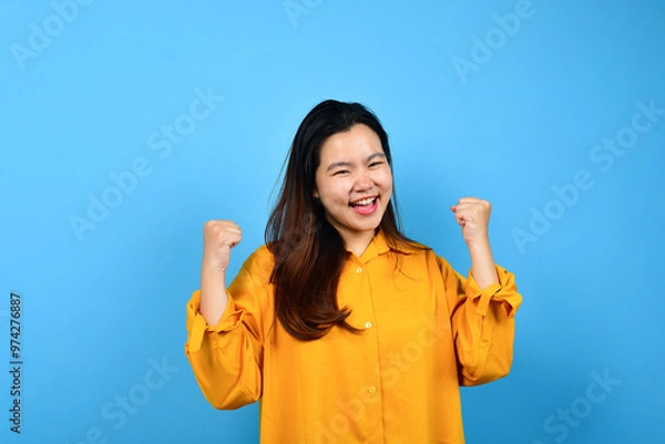 Obraz A young Asian woman with a happy successful expression wearing yellow shirt with copy space isolated on blue backround