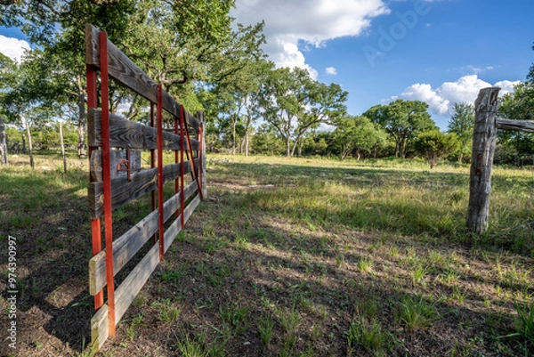 Fototapeta A gate with bent horseshoe handle, horizontal wooden rails and vertical angle metal stiles and diagonals mounted on a cedar hinge post along a Texas hill country ranch fence