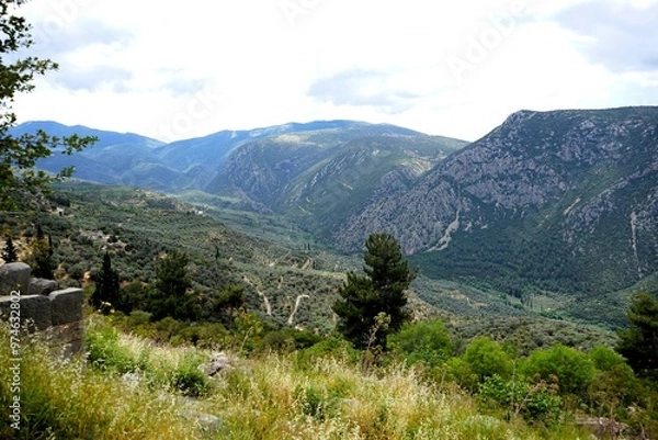 Fototapeta Ancient Greek ruins of the temple complex of the Oracle of Delphi in Greece with a breathtaking view of the panorama of the Pleistos River valley on a sunny summer's day 