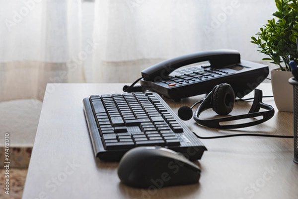 Fototapeta An office telephone nest to black computer keyboard and mouse are on a desk