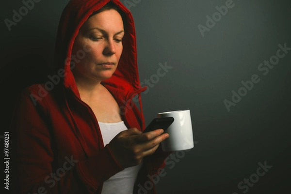 Fototapeta Beautiful red hooded woman drinking coffee and sending text mess