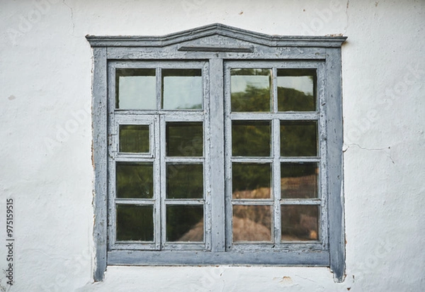 Fototapeta Close-up of an old grey wooden window on a white wall. Part of an old house with painted and weathered window