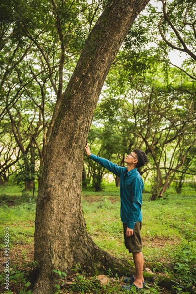 Fototapeta A man's hands gently touch the rough bark of a towering tree, symbolizing a deep connection with nature. In the forest, he embraces the importance of environmental care and protecting the planet.