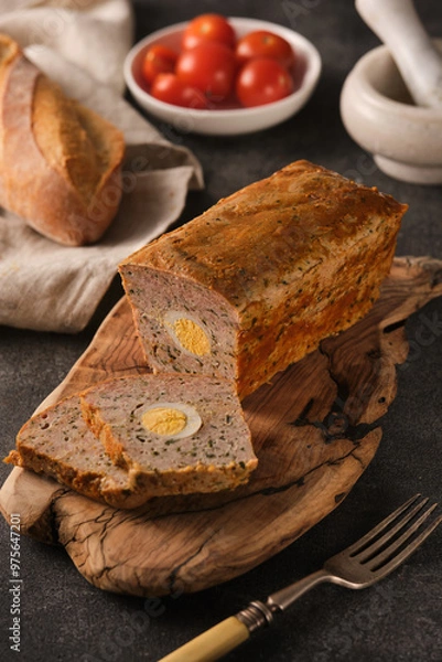 Obraz A rustic table showcasing a homemade meatloaf with boiled eggs, fresh bread, and cherry tomatoes under soft, natural light