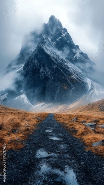 Obraz Misty mountain with a rocky peak, surrounded by fog, and a path leading towards it through grassy terrain