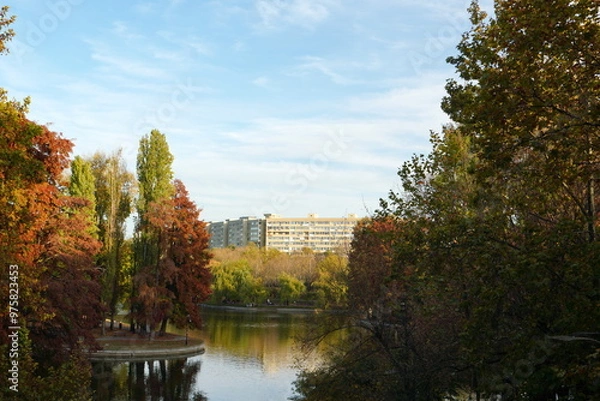 Fototapeta Beautiful autumn landscape with trees, lake and block of apartments in IOR park in Titan neighborhood in Bucharest, Romania
