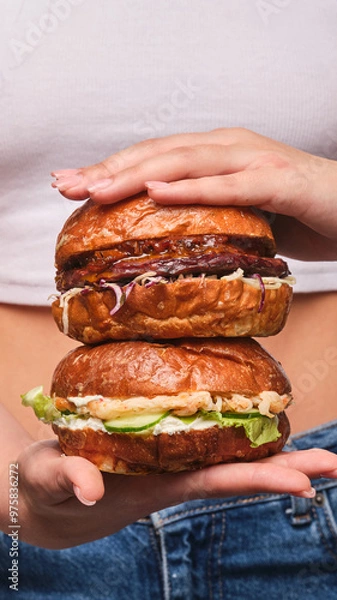 Obraz Delicious stacked burgers held by a smiling person against a casual backdrop, showcasing mouthwatering toppings and fresh ingredients at lunchtime