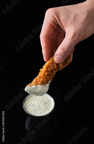 Obraz Crisp chicken tenders dipped in creamy sauce on a sleek black surface in a gourmet setting