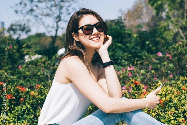 Fototapeta Young Asian lady in sunglasses with smartphone smiling and looking at camera
