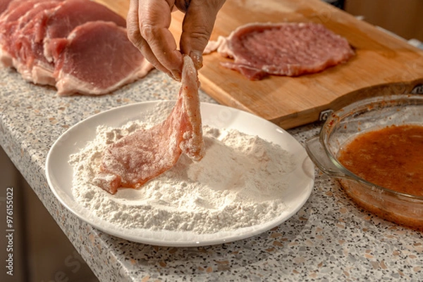 Fototapeta Cook dips pieces of beaten meat fillet in flour before further frying in a frying pan