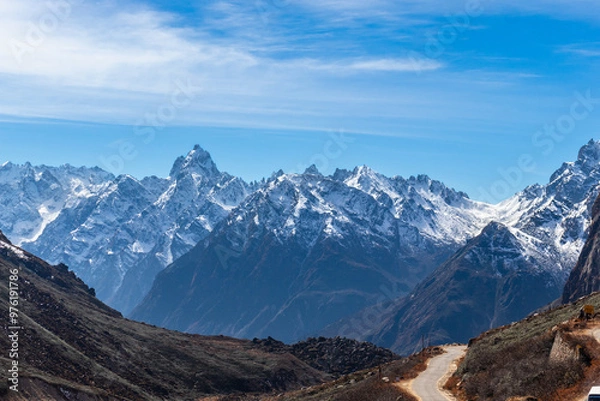 Obraz A stunning view of snow-capped mountains under a clear blue sky. Rugged peaks and a winding path create a picturesque scene, ideal for travel, adventure, nature, and outdoor themes, Sikkim, India