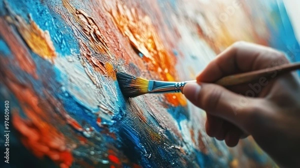 Fototapeta A detailed shot of a hand holding a paintbrush, with vibrant paint strokes on a canvas in the background