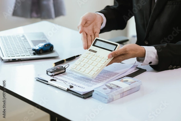 Fototapeta A satisfied customer signs paperwork at a car dealership, finalizing the purchase of a new vehicle. The salesman hands over the car key, completing the finance and insurance deal.
