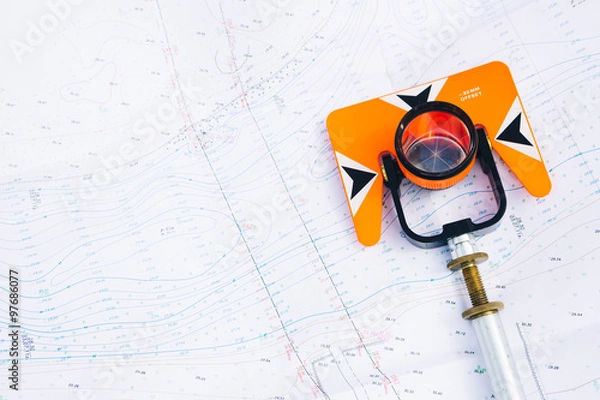 Fototapeta pomarańczowy pryzmat teodolitowy leży na tle geodezyjnych map obszaru