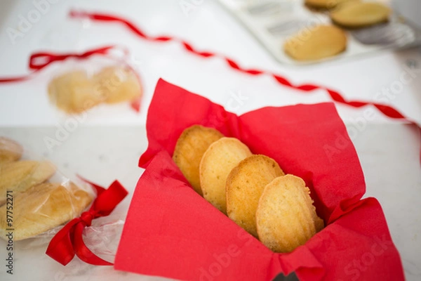 Fototapeta Madeleines in a red napkin on a white marble pastry board amid gift-wrapped sweets.