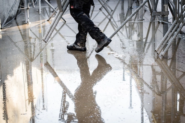 Fototapeta Construction site under water. Legs of a working man and his reflection in the water. Selective focus.