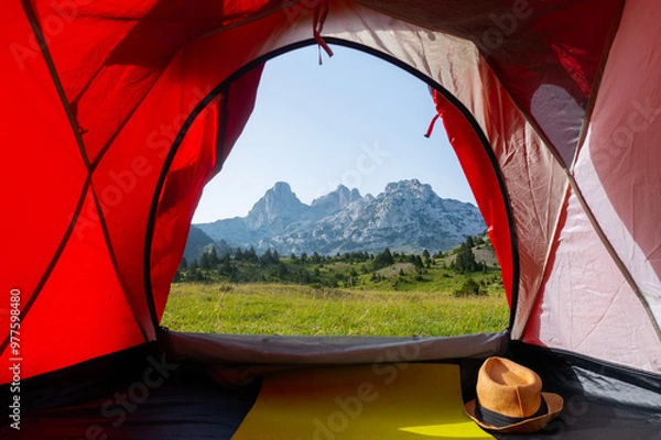 Fototapeta A beautiful view from the tent of a green meadow with rocky mountain peaks in the background