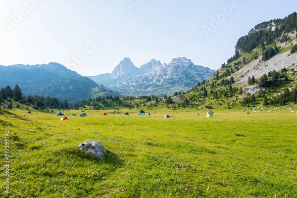 Fototapeta A valley full of tents of hikers camping on a mountain with a view of the peaks in the background