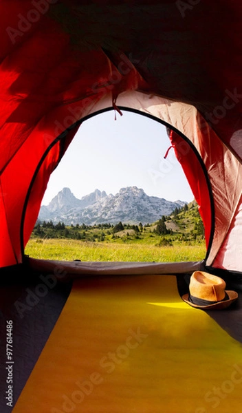 Fototapeta A beautiful view from the tent of a green meadow with rocky mountain peaks in the background