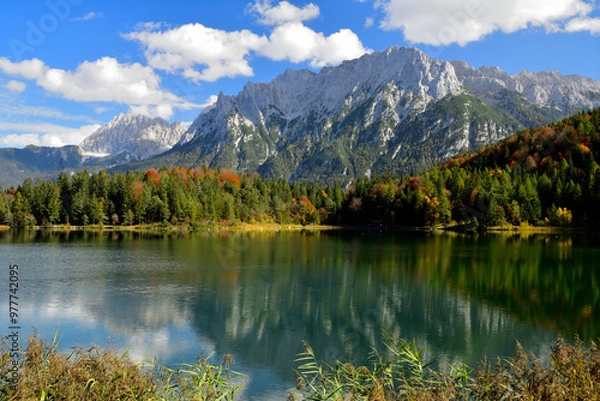 Obraz Ein traumhaft schönes Panoramabild aus den herbstlichen Alpen, mit einem idyllischen Bergsee und den aufragenden Berge unter einem Blau-Weißen Himmel.