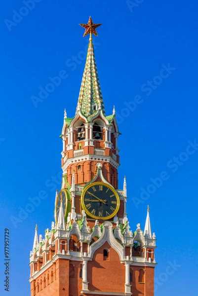Fototapeta The Spasskaya Tower of the Moscow Kremlin, with its iconic clock and spire, stands tall against a bright blue sky.
