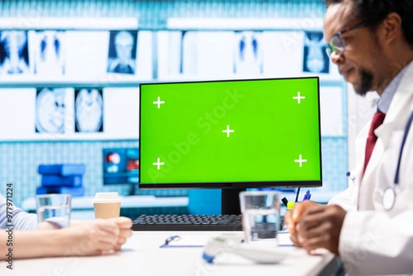 Fototapeta African american medic points at green screen on computer while he consults his patient, exploring treatment plans on health insurance. Physician gives medical advice to ill woman.