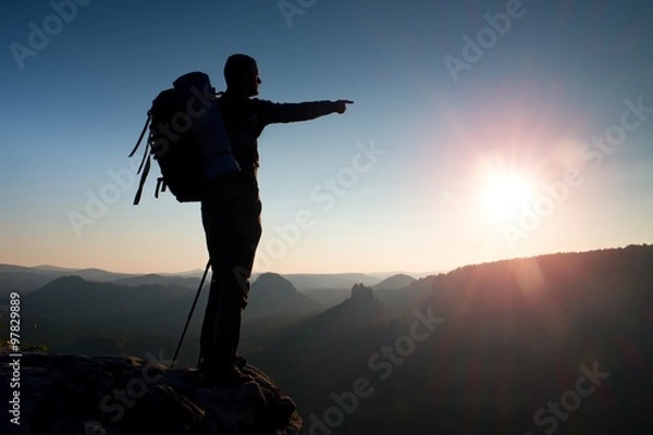 Fototapeta Sharp silhouette of a tall man on the top of the mountain with sun in the frame. Tourist guide in mountains
