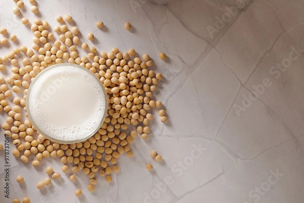 Fototapeta Top shot of fresh soy milk in a glass surrounded by scattered soybeans on marble background. 