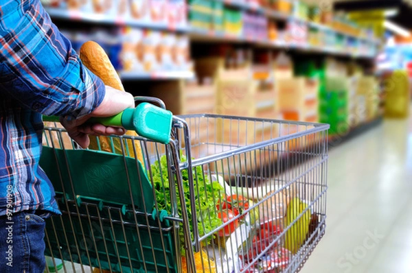 Obraz Mężczyzna pcha wózek na zakupy w przejściu supermarketu