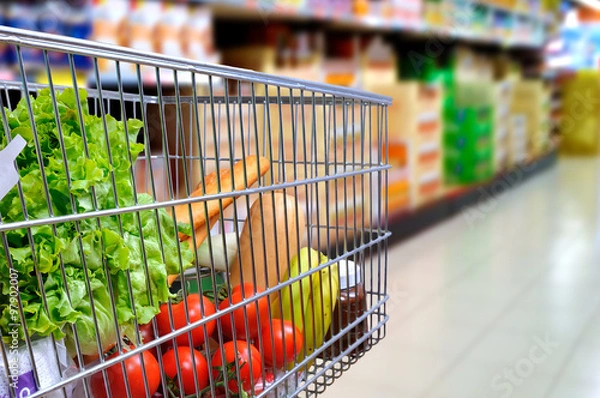 Obraz Wózek na zakupy pełen jedzenia w bocznym przechyleniu korytarza supermarketu