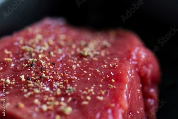 Fototapeta A close up portrait of the seasoning on a red raw steak being prepared or cooked in a frying pan. The delicious meat has salt and pepper on it for a perfect dinner or meal.